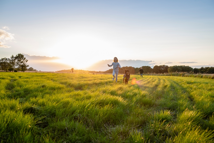 Kvinna springer över ett fält med sin hund i en solnedgång